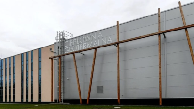 Geothermal power plant exterior with a wooden frame scaffolding and a sign reading 'CIEPLOWNIA GEOTERMALNA' on the wall