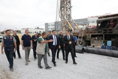 Group of men in business and work attire walking and talking near a large drilling rig on a gravel construction site.