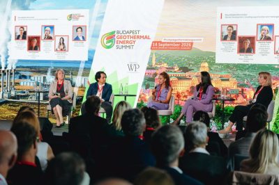Panel discussion at the Budapest Geothermal Energy Summit with four speakers onstage and a seated audience, bright backdrop showing event branding and skyline imagery.