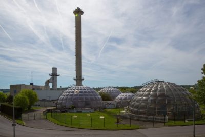 Meaux-energy-center-1024x683 | JeotermalHaberler - Jeotermal Haber Industrial facility featuring geodesic glass domes and a tall smokestack against a blue sky.